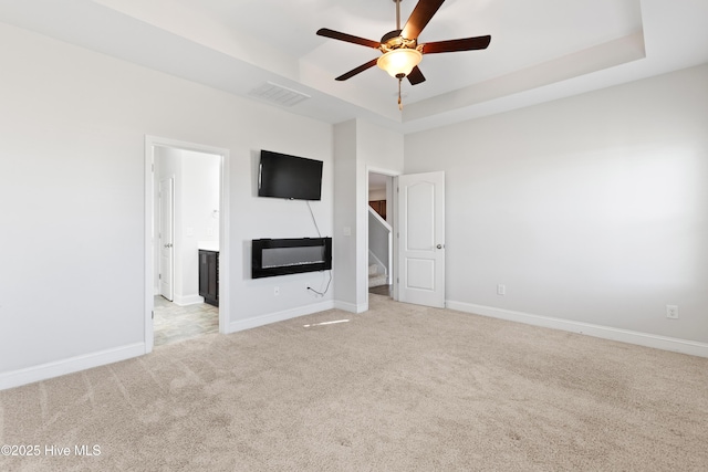 unfurnished living room featuring a raised ceiling, ceiling fan, and light colored carpet