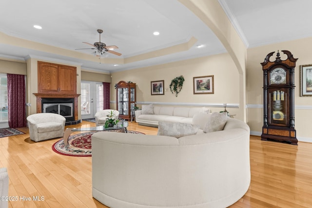 living room with french doors, a raised ceiling, ceiling fan, crown molding, and light hardwood / wood-style flooring