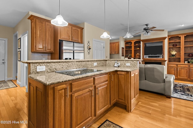 kitchen featuring stainless steel fridge, light stone counters, black electric cooktop, a kitchen island, and hanging light fixtures