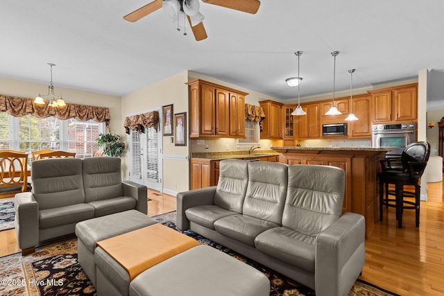 living room featuring light hardwood / wood-style flooring, ceiling fan with notable chandelier, and sink