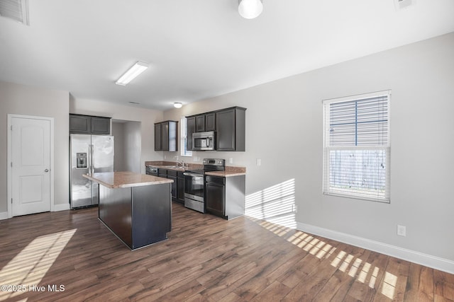 kitchen featuring appliances with stainless steel finishes, a center island, dark hardwood / wood-style flooring, and sink