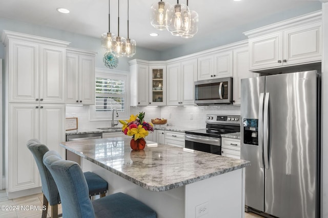 kitchen with stainless steel appliances, a kitchen island, sink, decorative light fixtures, and white cabinetry