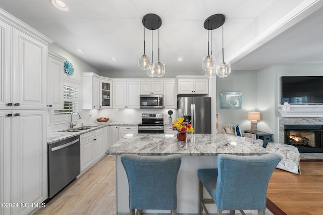 kitchen with a center island, sink, light stone countertops, appliances with stainless steel finishes, and white cabinetry