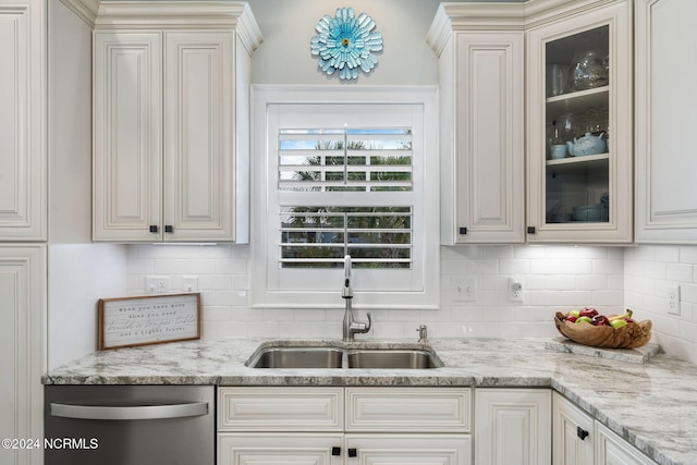 kitchen with light stone countertops, backsplash, stainless steel dishwasher, and sink