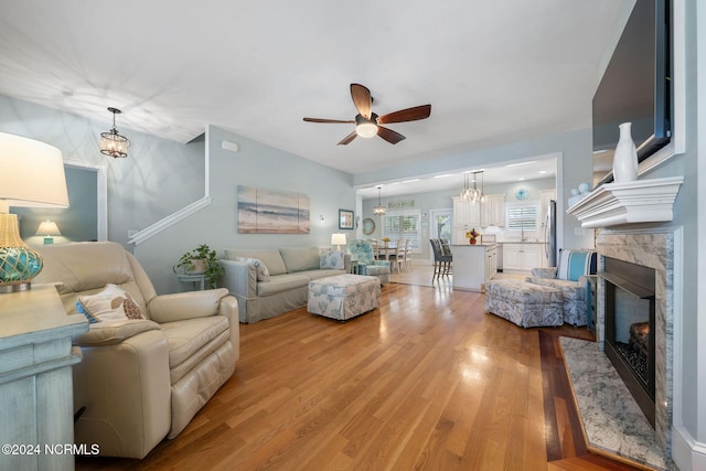 living room featuring a fireplace, ceiling fan with notable chandelier, and light wood-type flooring