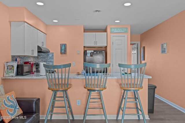 kitchen featuring black appliances, wood-type flooring, decorative backsplash, a kitchen bar, and white cabinetry