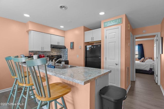 kitchen with white cabinetry, a kitchen bar, black refrigerator, backsplash, and light hardwood / wood-style flooring