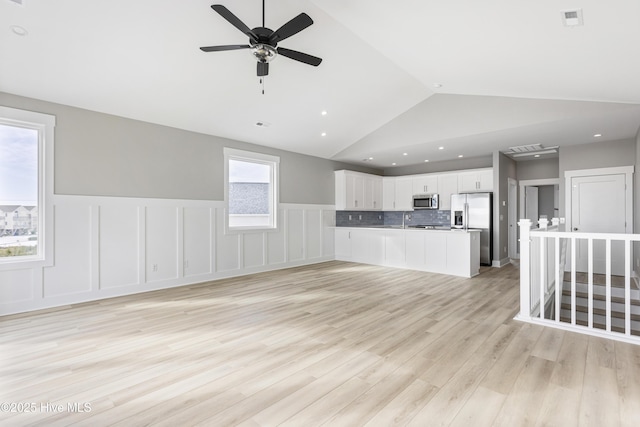 kitchen with lofted ceiling, stainless steel appliances, white cabinetry, open floor plan, and light wood-type flooring