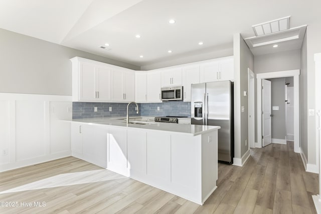 kitchen with light countertops, decorative backsplash, appliances with stainless steel finishes, white cabinets, and a peninsula