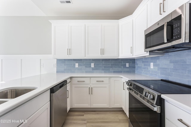 kitchen featuring decorative backsplash, white cabinets, light wood-style flooring, appliances with stainless steel finishes, and light countertops