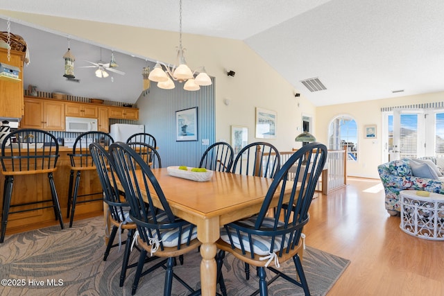 dining room with ceiling fan with notable chandelier, light wood-type flooring, lofted ceiling, and a textured ceiling