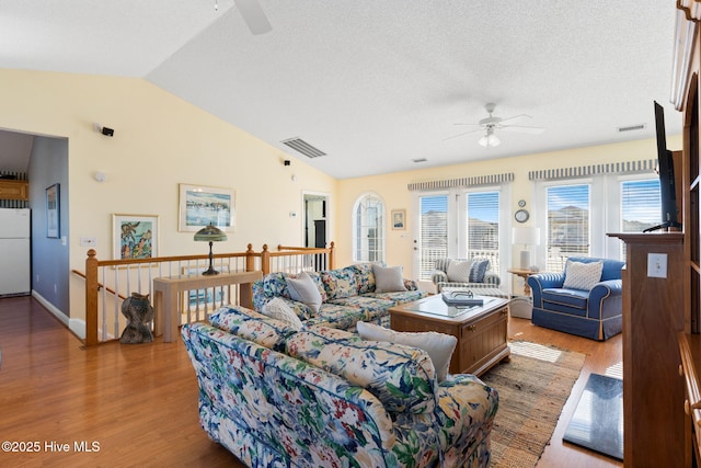 living room with a textured ceiling, vaulted ceiling, light hardwood / wood-style flooring, and ceiling fan