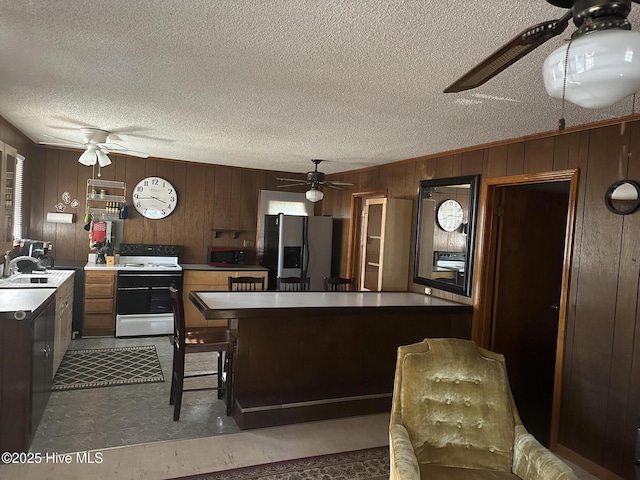 kitchen with sink, stainless steel fridge, wood walls, and white range with electric stovetop