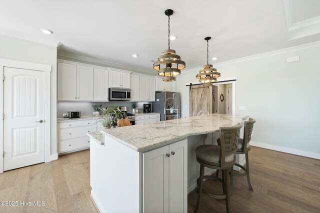 kitchen with white cabinetry, appliances with stainless steel finishes, a kitchen island with sink, and a barn door