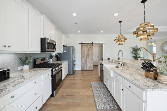 kitchen with decorative light fixtures, a barn door, backsplash, appliances with stainless steel finishes, and white cabinets