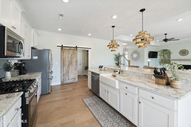 kitchen with a barn door, appliances with stainless steel finishes, decorative light fixtures, white cabinets, and sink