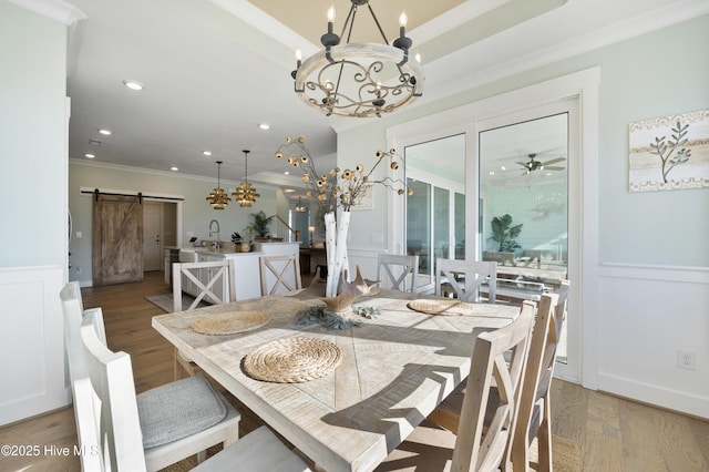 dining room featuring ceiling fan, a barn door, wood-type flooring, sink, and ornamental molding