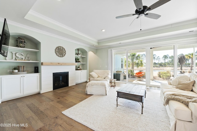 living room with ceiling fan, dark hardwood / wood-style flooring, a tray ceiling, and built in shelves