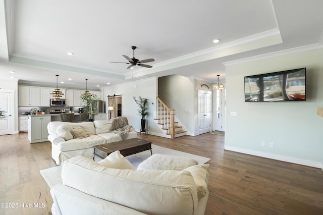 living room with light wood-type flooring, crown molding, a barn door, and a raised ceiling