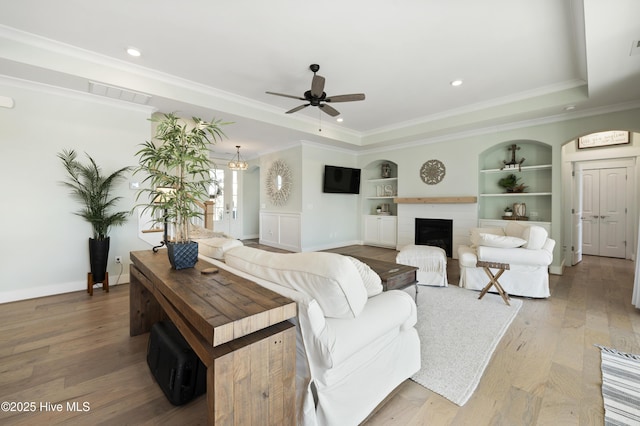 living room featuring ceiling fan, crown molding, a raised ceiling, and built in shelves