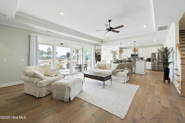 living room with ceiling fan, light wood-type flooring, and a tray ceiling