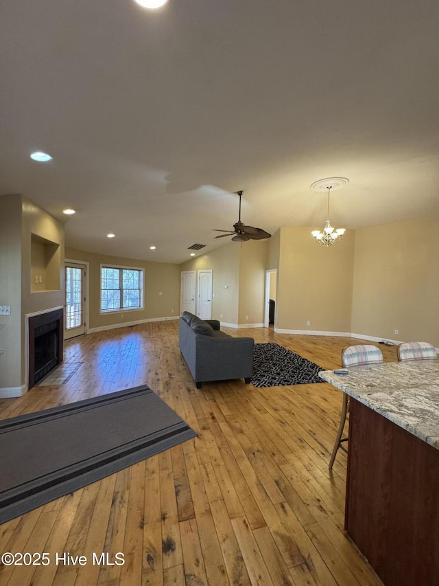 unfurnished living room featuring vaulted ceiling, light hardwood / wood-style floors, and ceiling fan with notable chandelier