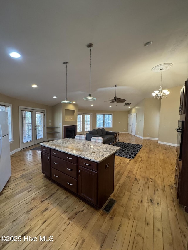 kitchen featuring hanging light fixtures, light hardwood / wood-style flooring, oven, a kitchen island, and ceiling fan with notable chandelier