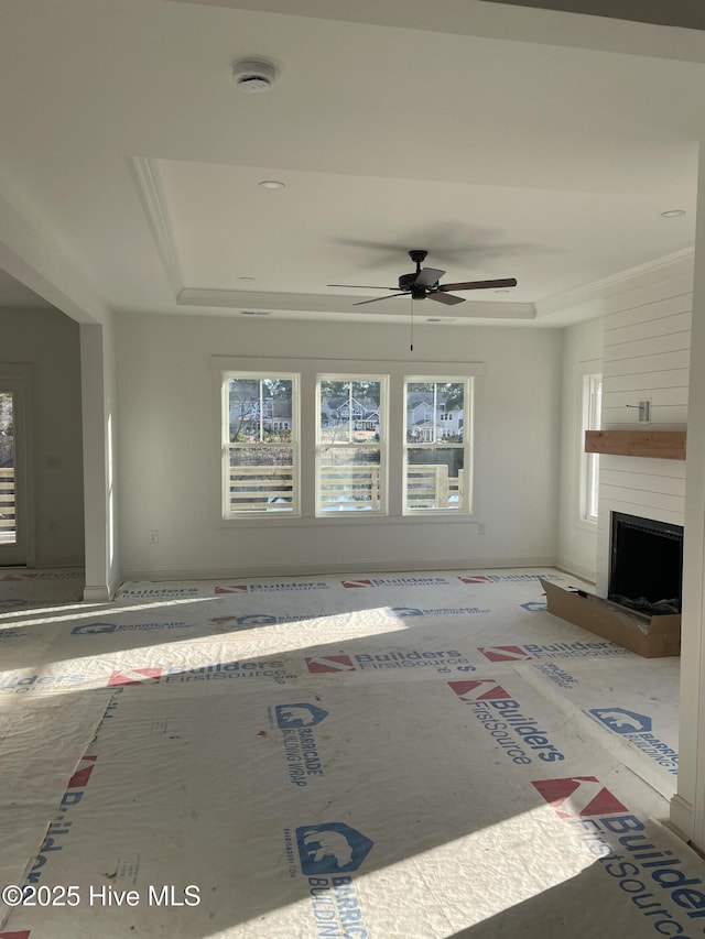 unfurnished living room with ceiling fan, a fireplace, and a tray ceiling