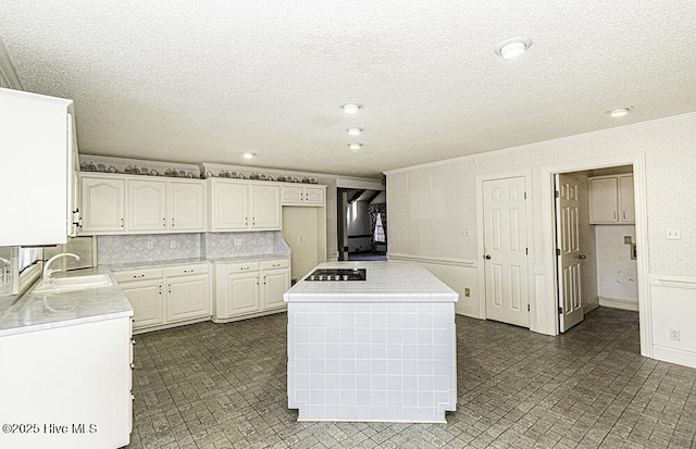 kitchen featuring ornamental molding, a textured ceiling, sink, a center island, and white cabinetry