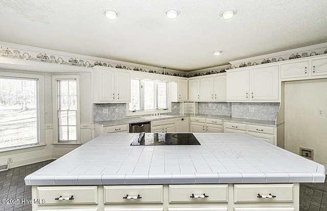 kitchen with backsplash, black electric cooktop, tile countertops, dishwasher, and white cabinetry