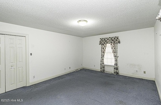 empty room with dark carpet and a textured ceiling