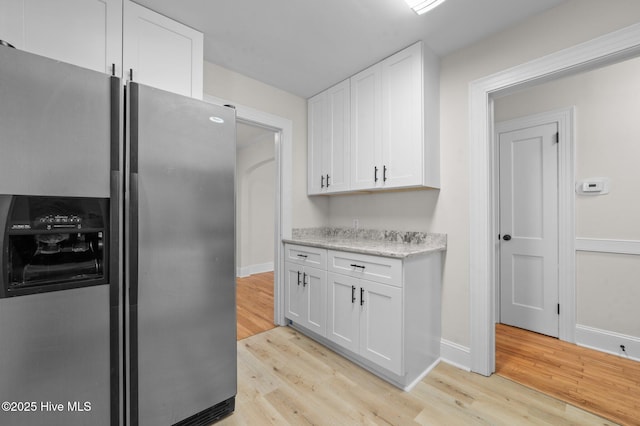 kitchen with stainless steel fridge, white cabinets, light stone counters, and light wood-type flooring