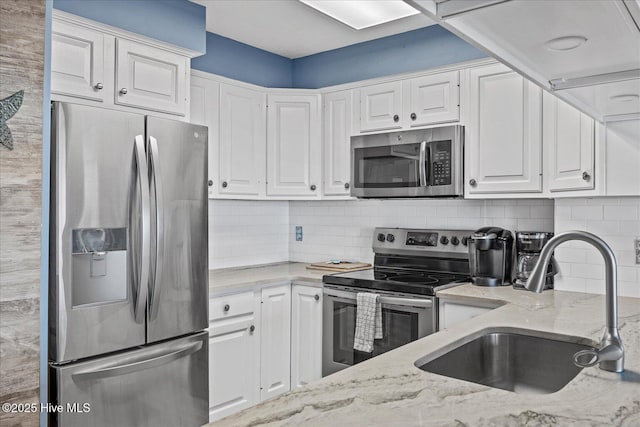 kitchen featuring sink, light stone counters, backsplash, white cabinets, and appliances with stainless steel finishes