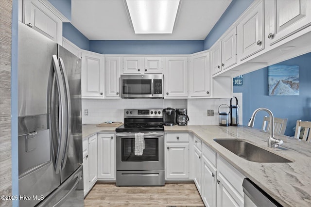 kitchen featuring decorative backsplash, light stone countertops, stainless steel appliances, sink, and white cabinets