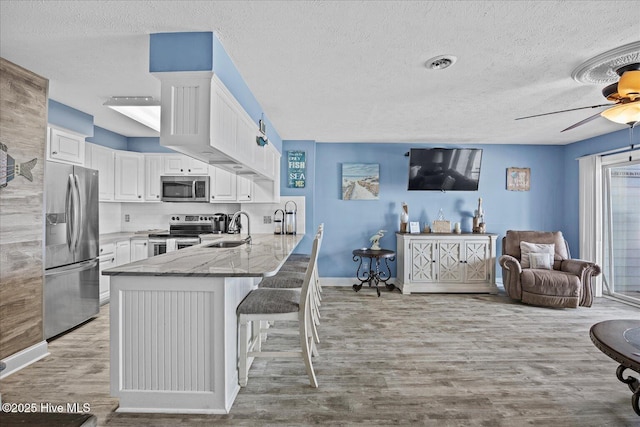 kitchen featuring kitchen peninsula, appliances with stainless steel finishes, white cabinets, and sink