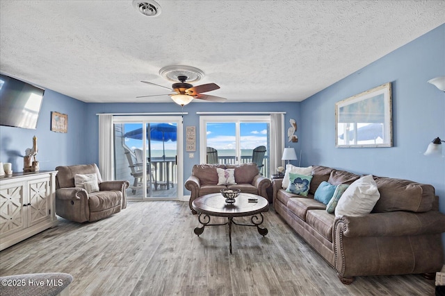 living room with a textured ceiling, light wood-type flooring, and ceiling fan