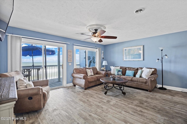 living room featuring ceiling fan, a water view, wood-type flooring, and a textured ceiling