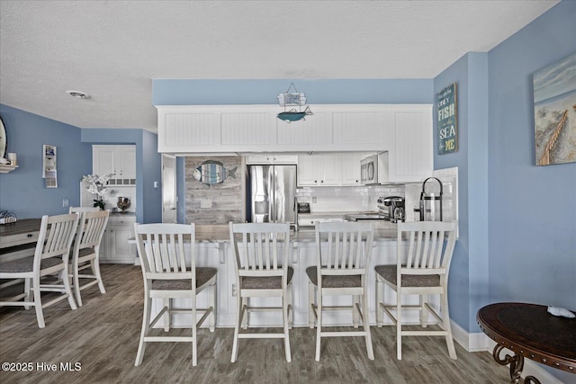 kitchen with stainless steel appliances, tasteful backsplash, a textured ceiling, a kitchen bar, and white cabinets