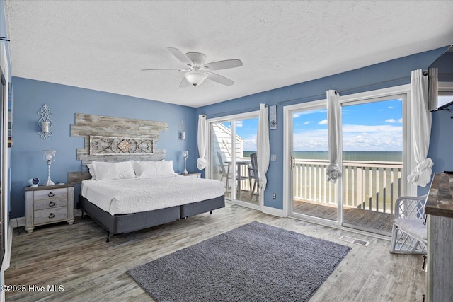 bedroom with hardwood / wood-style floors, a water view, ceiling fan, access to exterior, and a textured ceiling