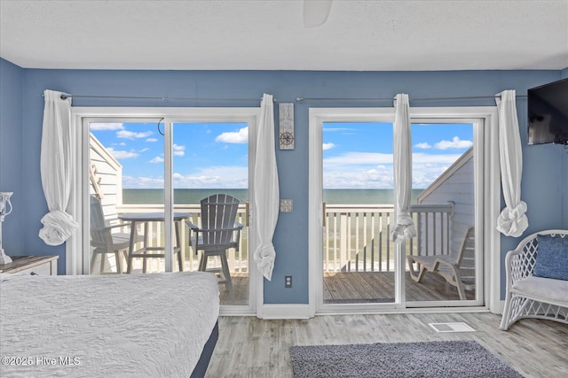 bedroom with access to exterior, hardwood / wood-style floors, a water view, and a textured ceiling