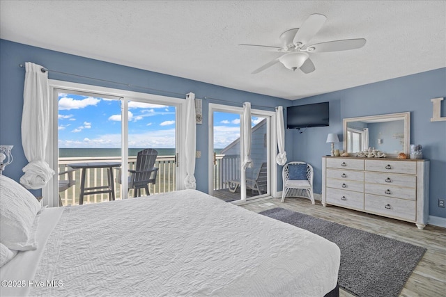 bedroom featuring hardwood / wood-style floors, access to outside, a water view, ceiling fan, and a textured ceiling