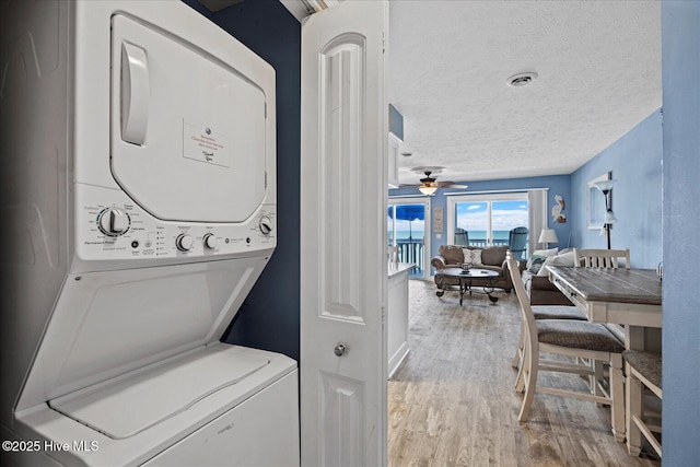 clothes washing area featuring hardwood / wood-style floors, a textured ceiling, stacked washing maching and dryer, and ceiling fan