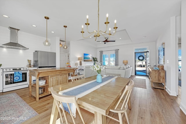 dining space featuring ceiling fan with notable chandelier, light hardwood / wood-style floors, and a raised ceiling