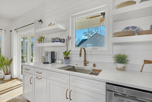 kitchen with sink, dishwasher, light hardwood / wood-style floors, white cabinetry, and wood walls