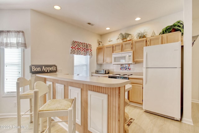 kitchen with light brown cabinetry, white appliances, a healthy amount of sunlight, and backsplash