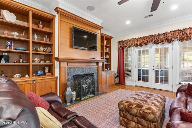 living room featuring ornamental molding, ceiling fan, a premium fireplace, light wood-type flooring, and french doors