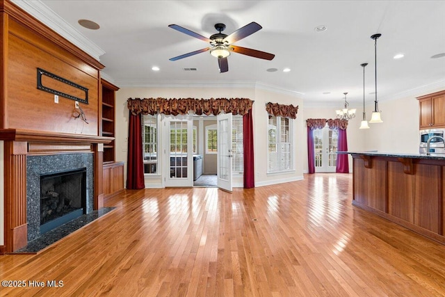 unfurnished living room featuring crown molding, a fireplace, ceiling fan with notable chandelier, and light wood-type flooring