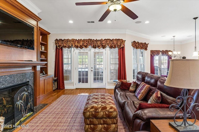 living room with french doors, wood-type flooring, ornamental molding, a high end fireplace, and ceiling fan with notable chandelier