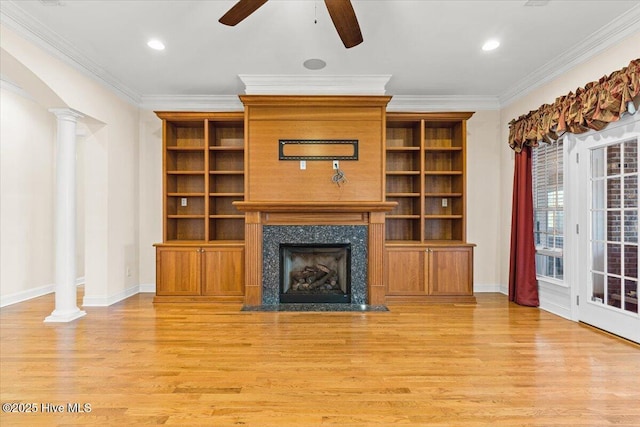 unfurnished living room featuring a fireplace, decorative columns, ceiling fan, crown molding, and light wood-type flooring