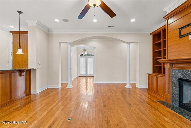 unfurnished living room with light wood-type flooring, ornamental molding, built in features, a premium fireplace, and decorative columns